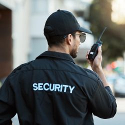 Radio, man and a security guard or safety officer outdoor on a city road for communication. Back of a person with a walkie talkie on urban street to report crime for investigation and surveillance.